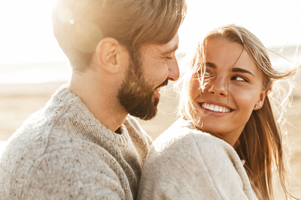 Close up of a smiling beautiful young couple embracing while standing at the beach