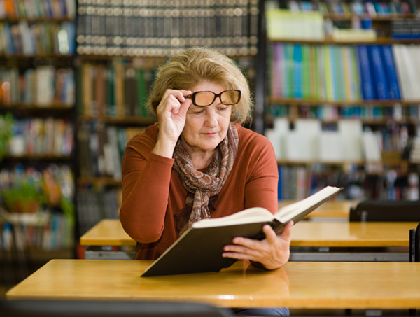 An elderly woman with glasses reads a book